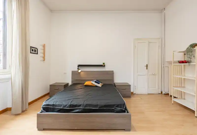 Dormitorio luminoso y minimalista con cama doble centrada, mesitas a juego y luz natural de una gran ventana.
