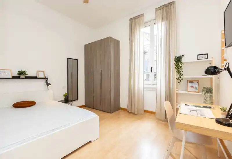 Dormitorio luminoso y minimalista con cama doble, armario y escritorio junto a la ventana — ideal para estudiante o profesional.