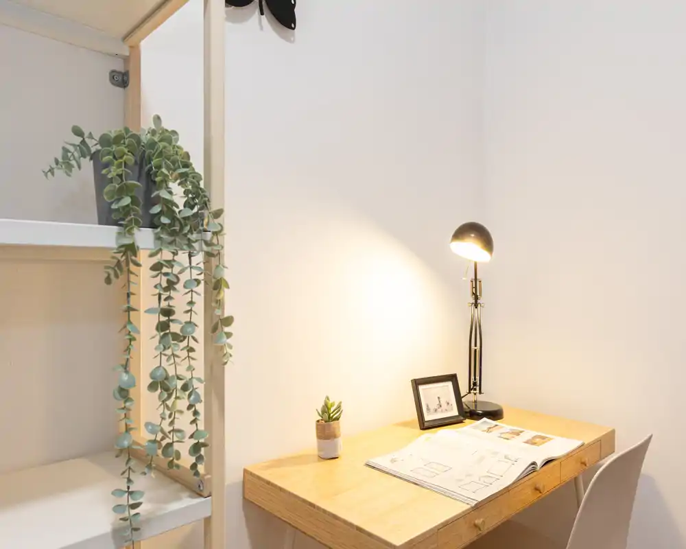 Zona luminosa y minimalista con mesa de madera, lámpara de trabajo, silla y pequeñas plantas — un espacio de trabajo ordenado o un rincón de comedor informal con luz cálida.