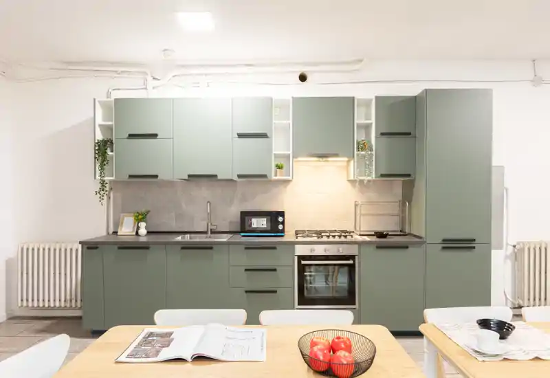 Cucina moderna e luminosa con pensili verdi, forno incassato e piano cottura a gas, lavabo e tavolo apparecchiato in primo piano — perfetta per annunci che puntano su uno spazio cucina funzionale e contemporaneo.