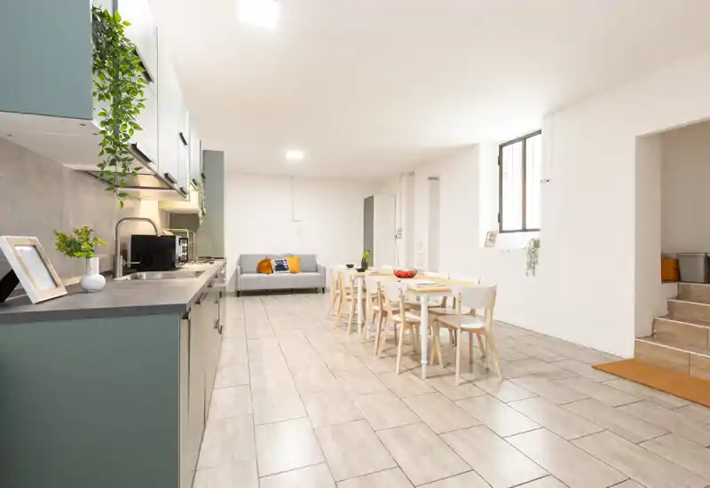 Ampio e luminoso open space con cucina moderna a sinistra, tavolo da pranzo per sei e divano confortevole — perfetto per soggiorni conviviali.