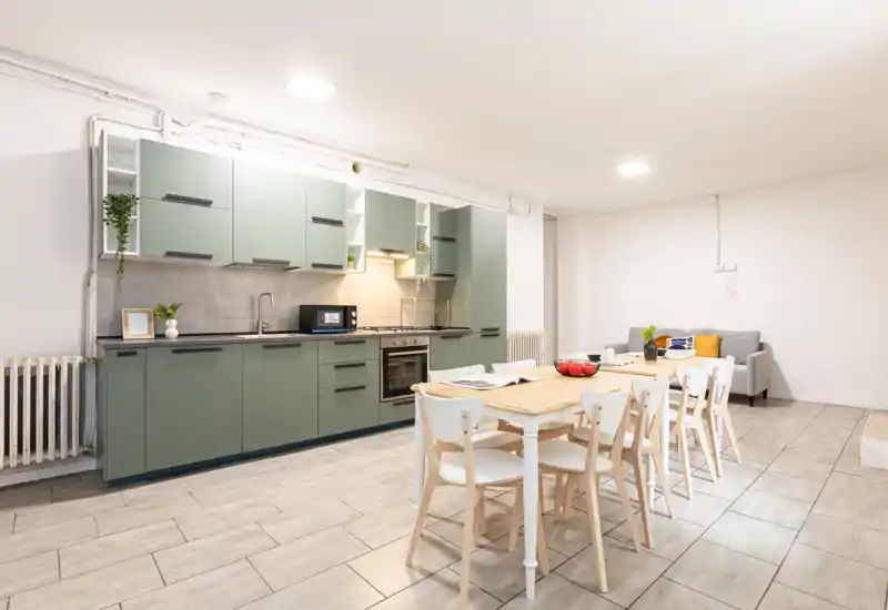 Cucina moderna a vista con pensili verde salvia, forno e microonde integrati e tavolo da pranzo in legno per sei persone; luminosa, pulita e ben arredata per annunci.