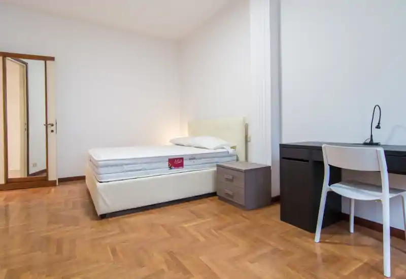 Bright, minimalist bedroom with a neatly made single bed, bedside table and a study desk—ideal for a student or single occupant.