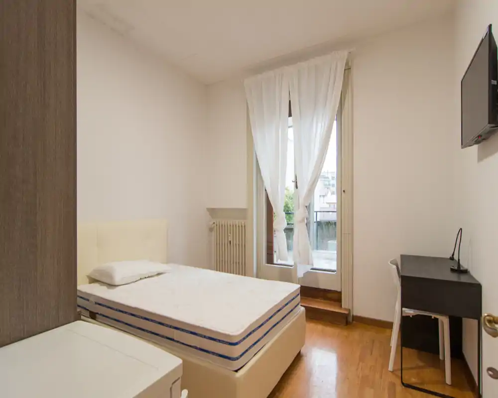 Camera singola luminosa e minimal con letto comodo, scrivania e porta sul balcone che garantisce luce naturale — ideale per uno studente o un single.