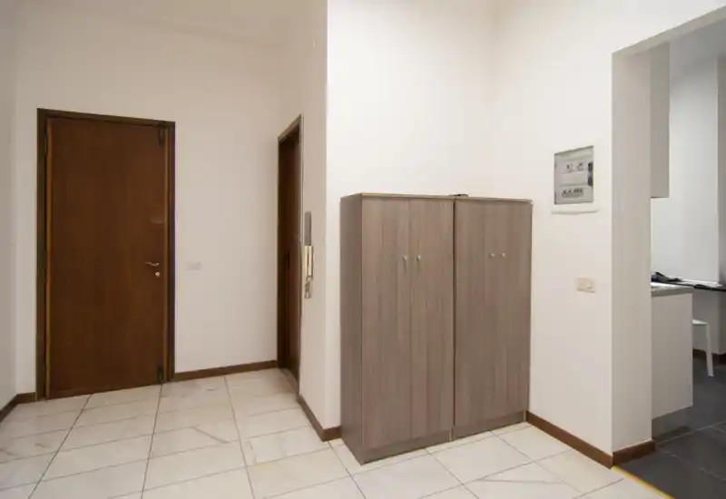 Clean, well-lit entrance hallway with tiled floor, wooden doors and a compact storage cabinet near the doorway.