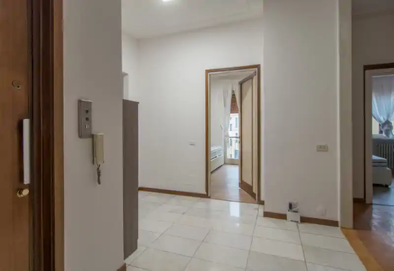 Bright entrance/hallway with tiled floor, visible intercom on the wall and doorways leading to adjacent rooms. Good natural light and neutral decor make it suitable for a listing’s entryway photo.