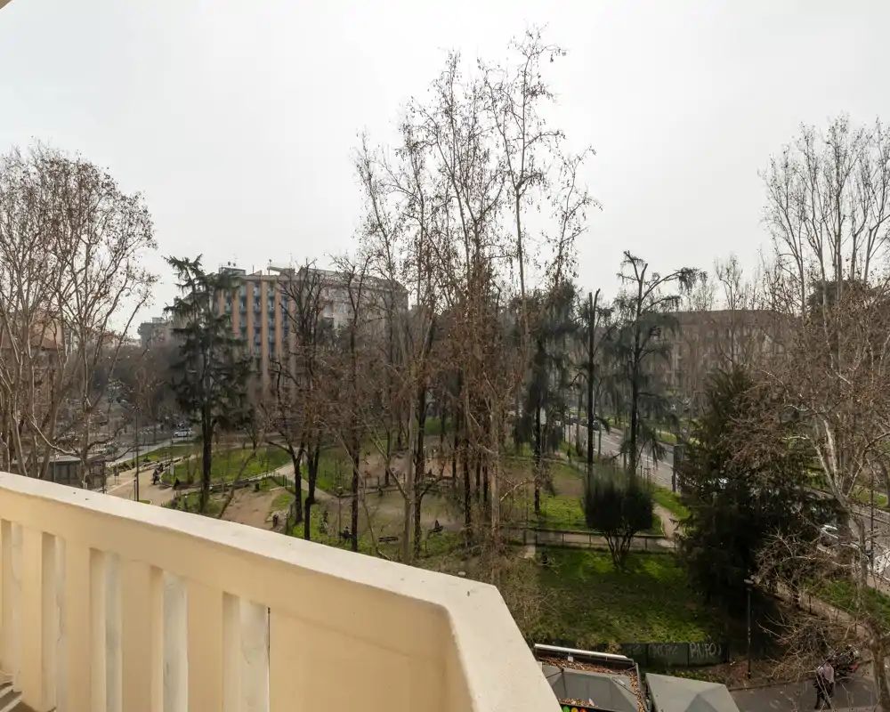 Vistas desde el balcón hacia un parque arbolado y edificios alrededor; entorno urbano tranquilo con zonas verdes visibles desde la terraza.