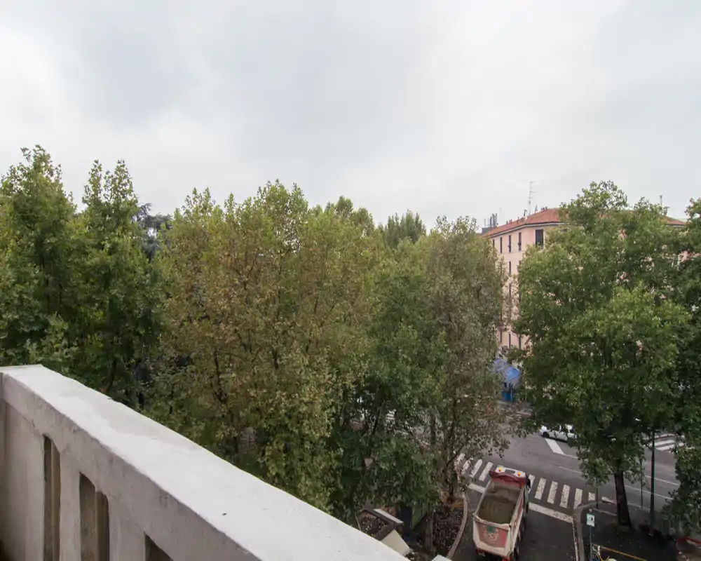 Balcone con vista su alberi frondosi e una strada; ideale per evidenziare lo spazio esterno e il verde del quartiere.