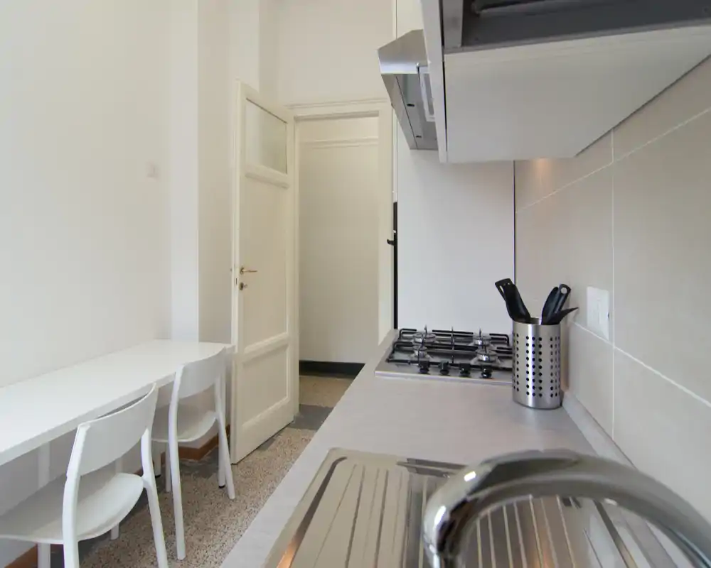 Cucina compatta e moderna con lavello in acciaio, piano cottura a gas e piccolo tavolo con sedie — luminosa, pulita e funzionale per l'uso quotidiano.