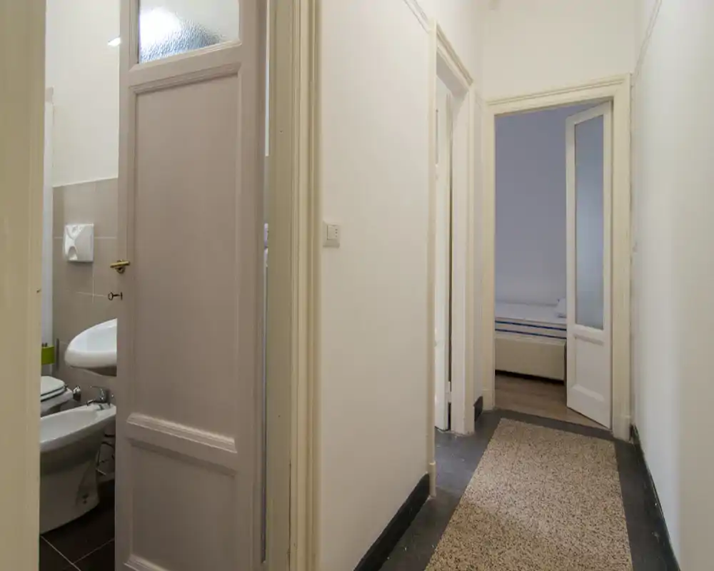 Ingresso/corridoio stretto con più porte; bagno visibile a sinistra e una camera avanti. Arredamento neutro e illuminazione funzionale, utile per descrivere la disposizione dell'appartamento.