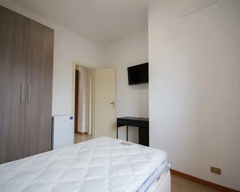 Dormitorio sencillo y luminoso con colchón visible, armario y televisor en la pared — estilo limpio y neutro apto para anuncios.