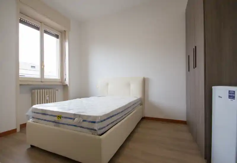 Dormitorio luminoso y minimalista con cama individual tapizada moderna, gran armario y luz natural desde la ventana. La decoración neutra y las líneas limpias crean un espacio tranquilo y listo para entrar a vivir.