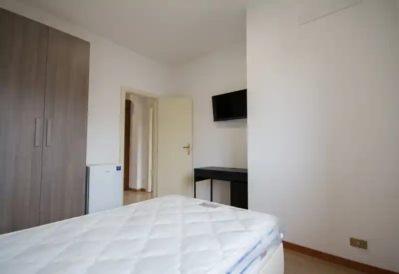 Dormitorio sencillo y luminoso con colchón visible, armario y televisor en la pared — estilo limpio y neutro apto para anuncios.