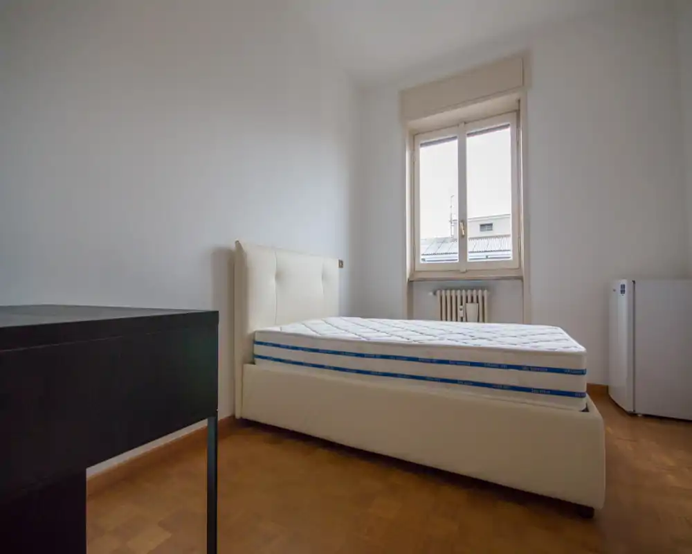 Minimal, bright bedroom with a modern upholstered bed and natural light from a large window. Simple hardwood floor and neutral walls create a calm, ready-to-personalize space.