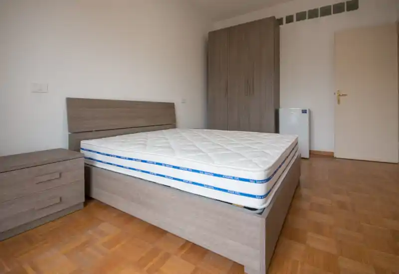 Dormitorio luminoso y despejado con cama completamente visible, mesita y armario de madera a juego y suelo de parquet — ideal para anuncios de alquiler que muestran la zona de descanso amueblada.