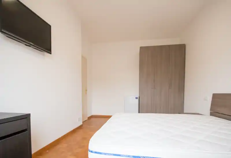 Bright, minimal bedroom with a large mattress in the foreground, a wooden wardrobe and simple modern furniture — ideal for a clean, unfurnished listing photo.