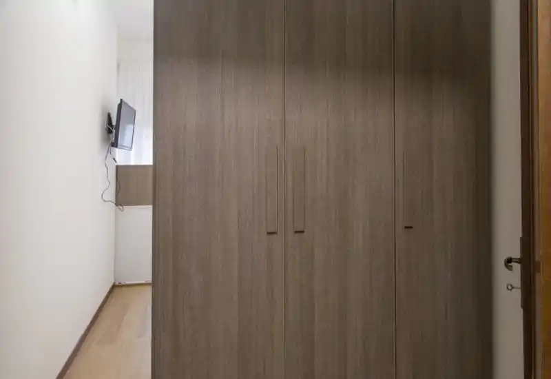 Image shows a large built-in wardrobe occupying the frame; the surrounding space is narrow and only a small wall-mounted TV and a sliver of floor are visible. The photo focuses on closet doors rather than a clearly identifiable room function.