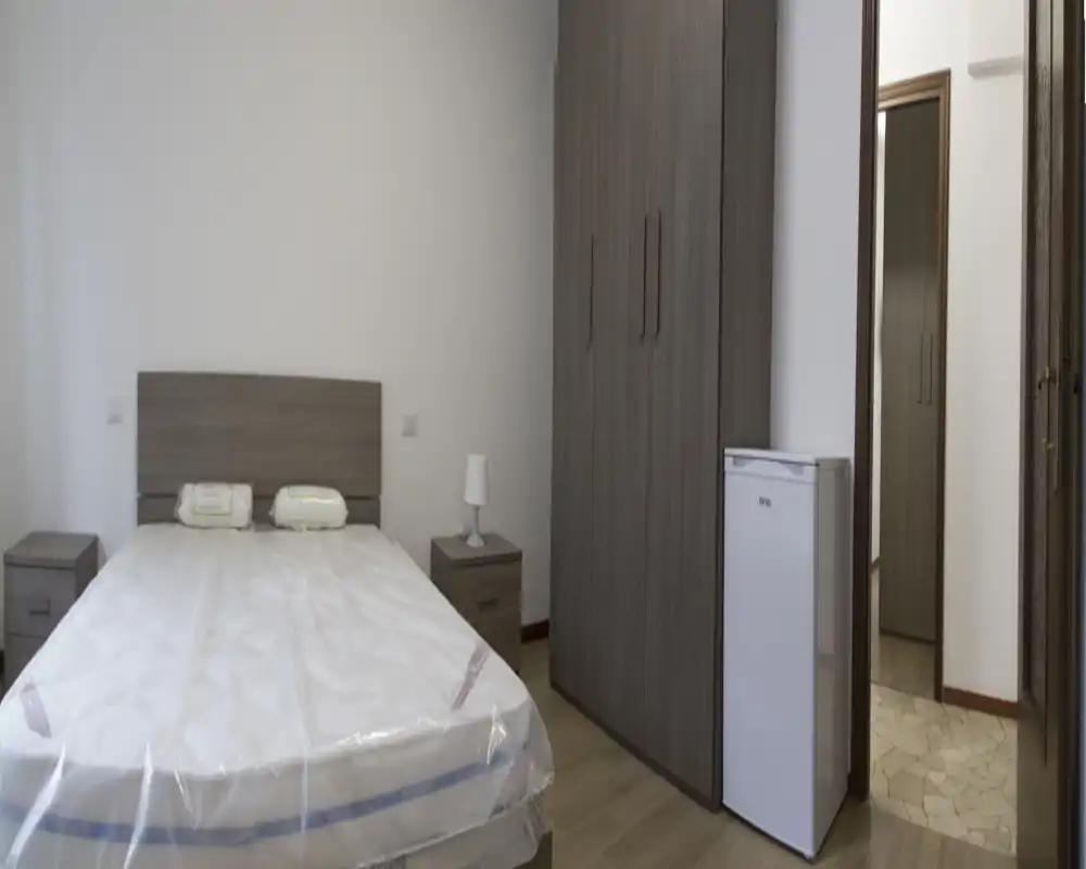 Camera da letto luminosa e arredata in modo semplice con letto matrimoniale, comodini coordinati e un ampio armadio. Toni neutri e linee pulite ideali per annunci in affitto.