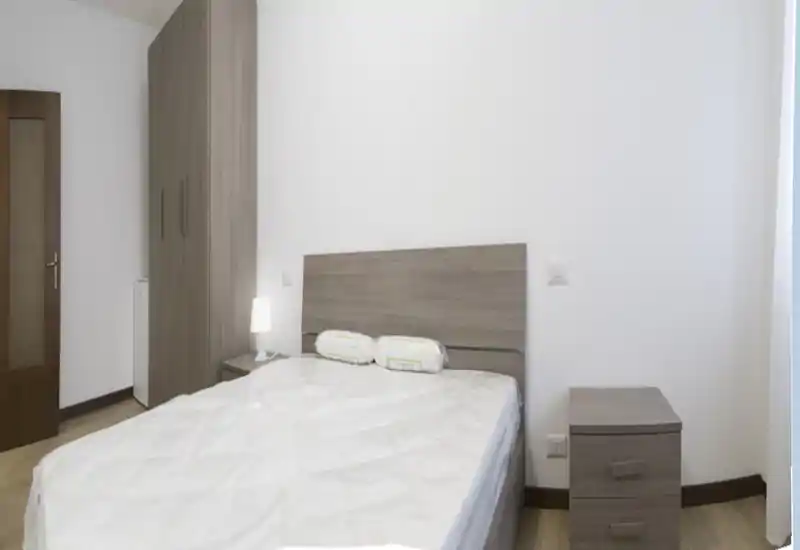 Chambre lumineuse et sobrement meublée avec lit double, tête de lit et table de chevet assorties, armoire et lampe de chevet — style neutre et propre, idéal pour une annonce.