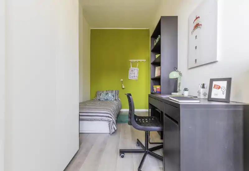 Camera compatta e ben arredata con letto singolo, scrivania e parete verde a contrasto; luminosa, moderna e ordinata — perfetta per studenti o soggiorni brevi.