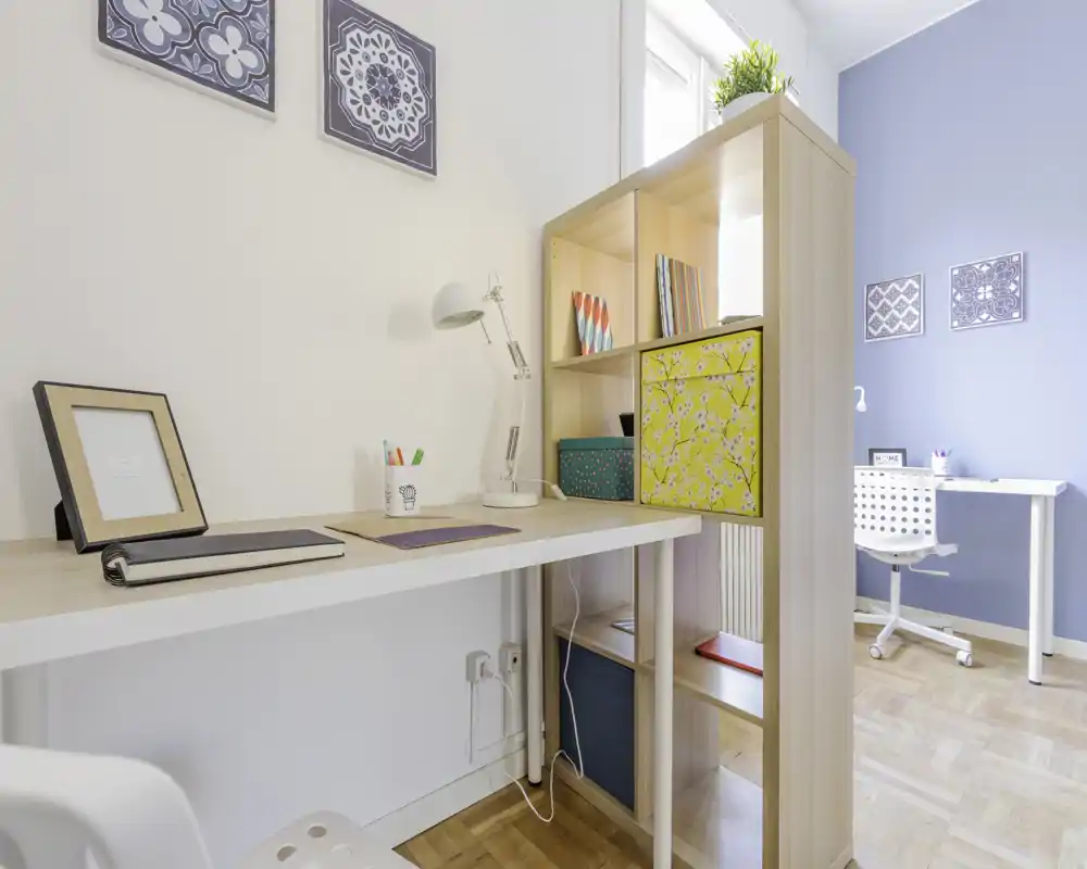 Rincón de oficina en casa luminoso y moderno con dos escritorios blancos, estantería y azulejos decorativos en la pared — un espacio de trabajo ordenado y bien iluminado, ideal para teletrabajo o estudio.