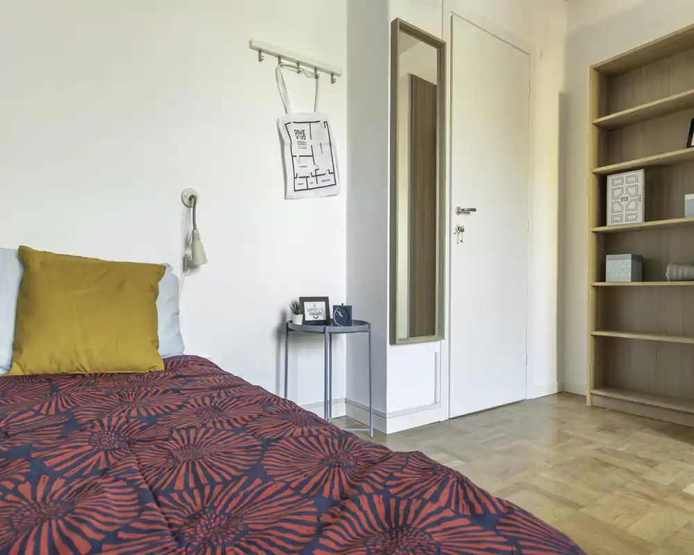 Dormitorio luminoso y ordenado con edredón estampado, mesita y espejo en la pared — un espacio acogedor y bien iluminado, ideal para alquileres de corta estancia.