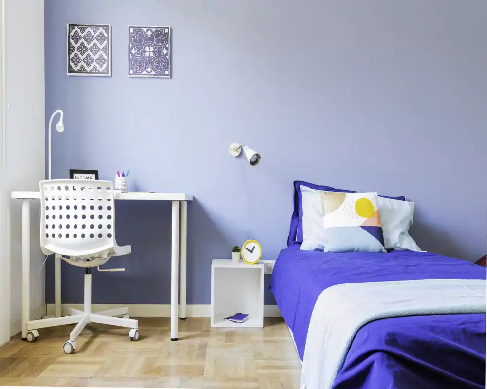 Dormitorio individual luminoso y bien decorado con colcha azul, cojines decorativos y un escritorio compacto — ideal para estudiantes o alquiler individual.