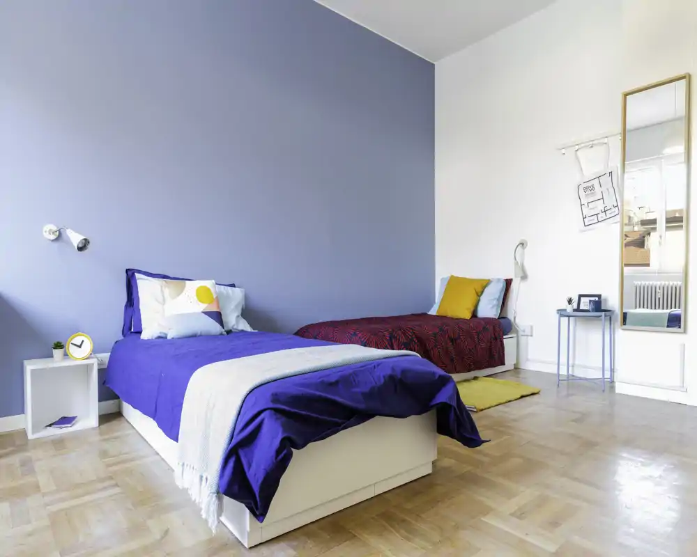 Dormitorio luminoso y moderno con dos camas individuales, ropa de cama elegante y una pared azul; ideal para estancias compartidas o invitados.