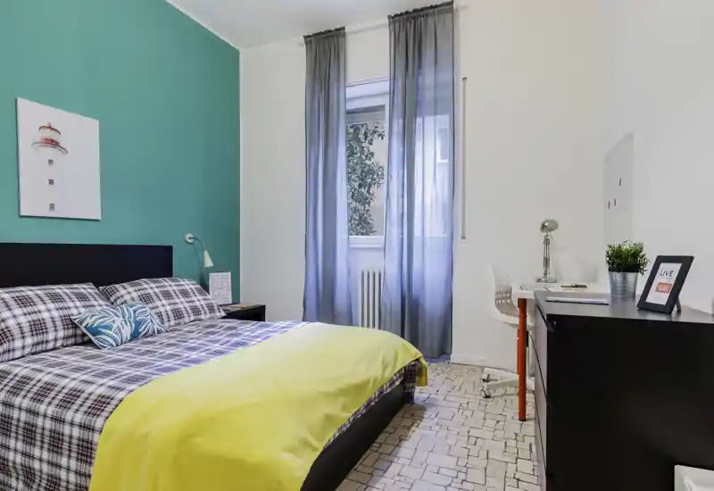 Bright, well-styled bedroom with a double bed, colorful accent wall and a desk by the window. Natural light and coordinated textiles create a welcoming atmosphere ideal for listings.