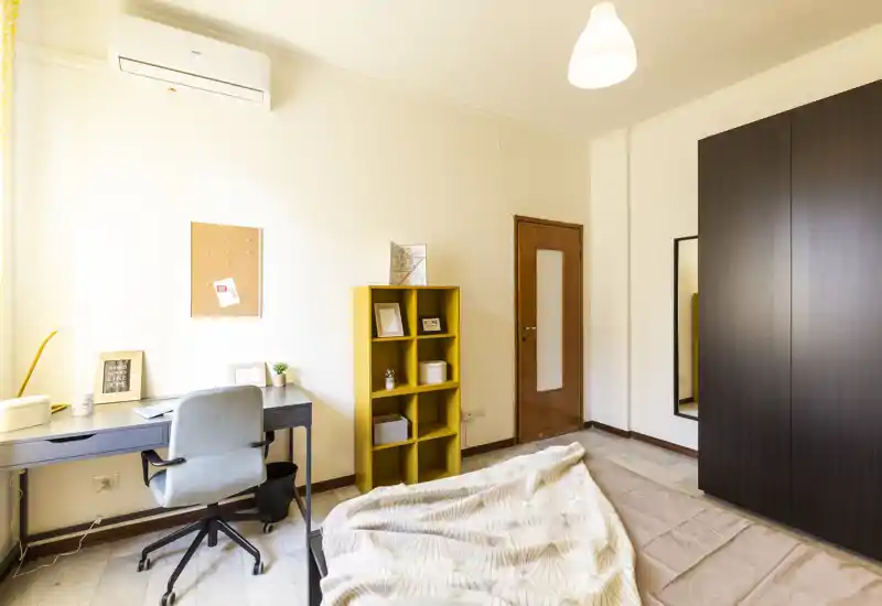 Camera da letto luminosa e ben arredata con letto visibile, angolo studio con scrivania e sedia, armadio e scaffale decorativo — perfetta per un annuncio in affitto che evidenzia comfort e funzionalità.