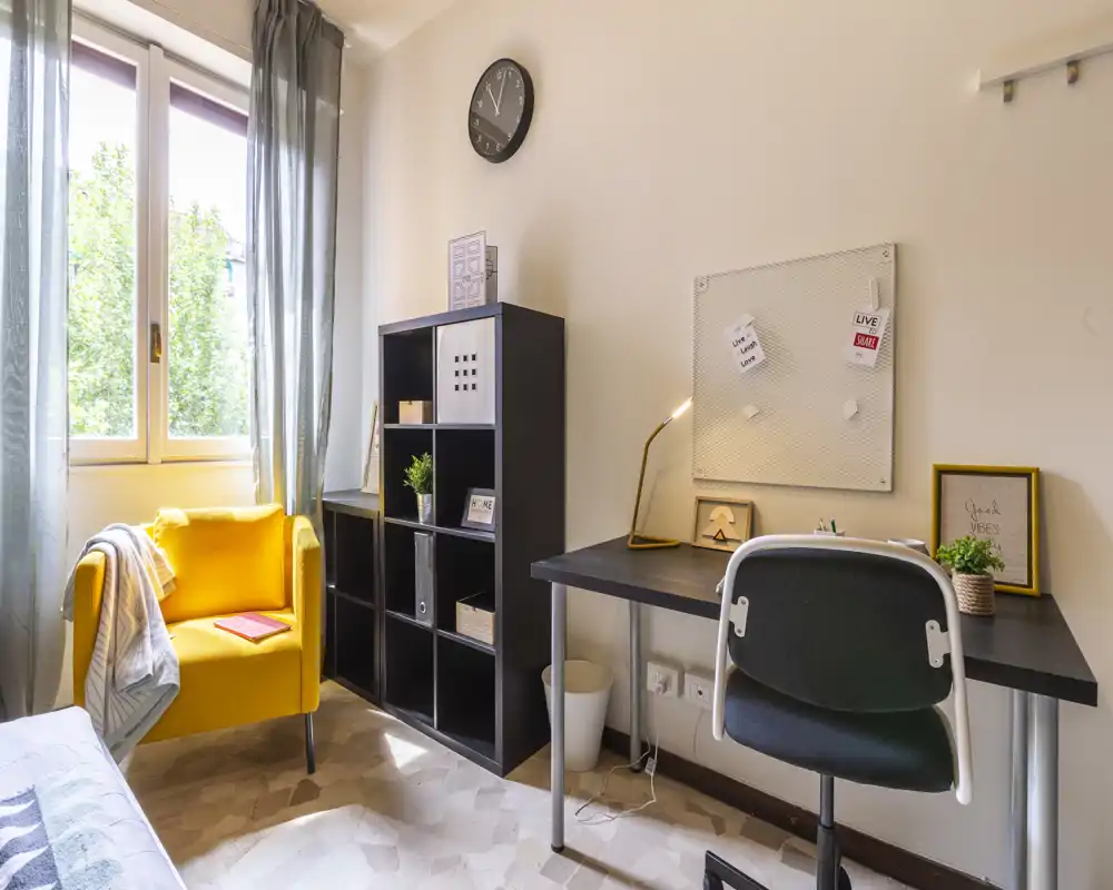 Bright, cozy bedroom corner with a study desk and a yellow armchair by the window; ideal for a student or remote worker seeking a sunny workspace.