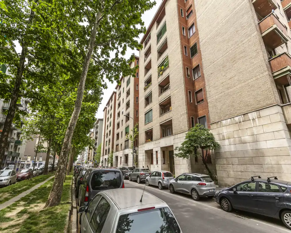 Street-facing urban exterior with parked cars, a tree-lined sidewalk and mid-rise residential buildings — ideal to show the neighbourhood and street access.