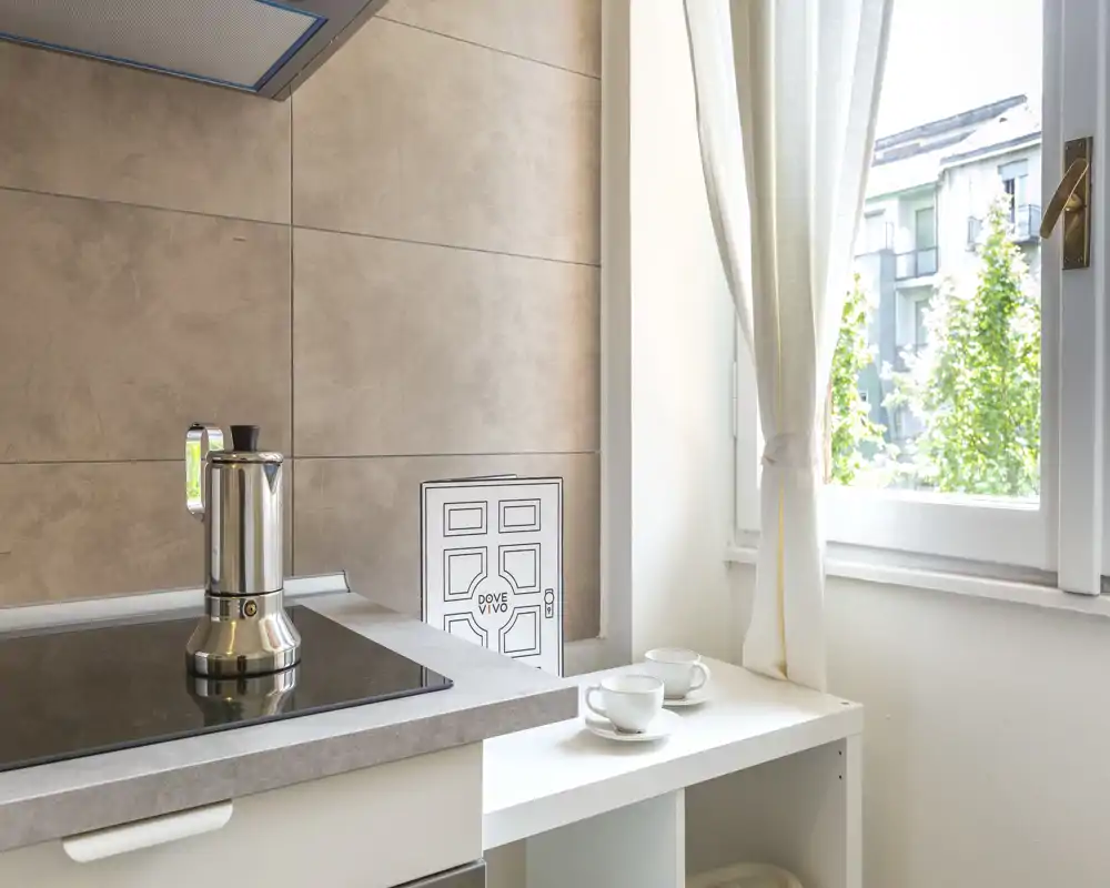Bright modern kitchenette corner with an induction hob, stovetop espresso maker and two cups by a sunny window, ideal for a compact city apartment.