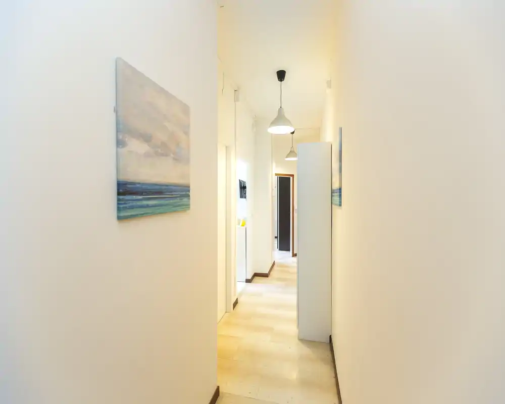 Bright, narrow hallway with neutral walls, pendant lights and artwork — a welcoming entrance corridor connecting rooms.