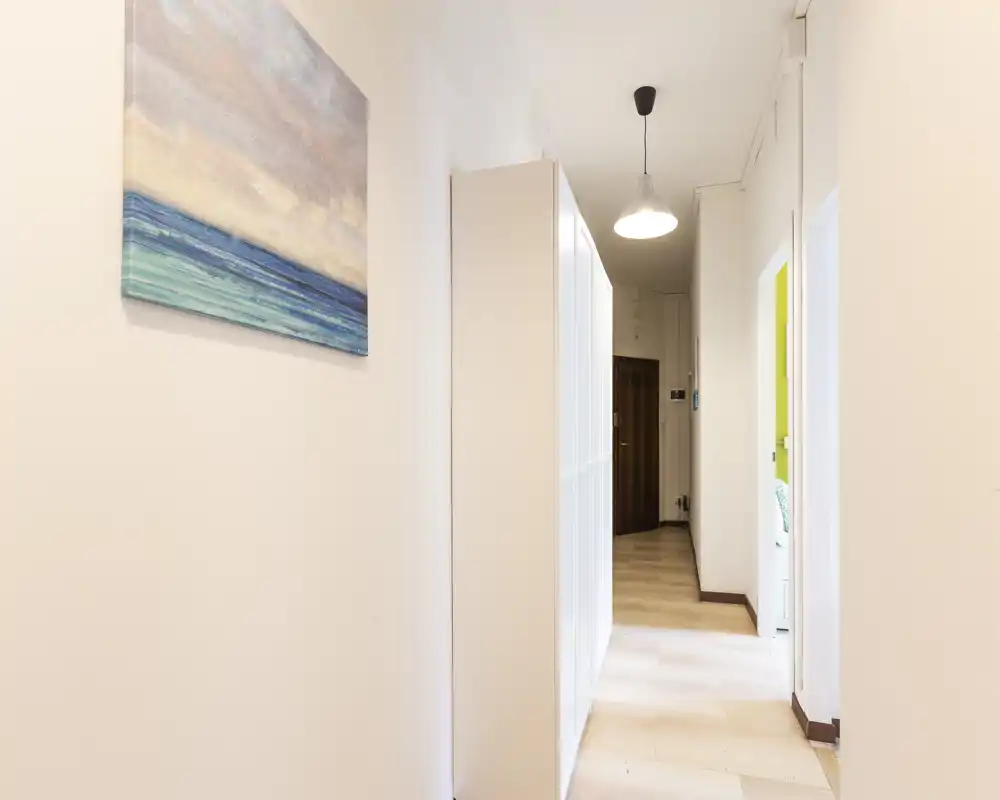 Bright, narrow entrance hallway with light-colored walls, built-in storage and a pendant light; clean and welcoming access to the apartment.