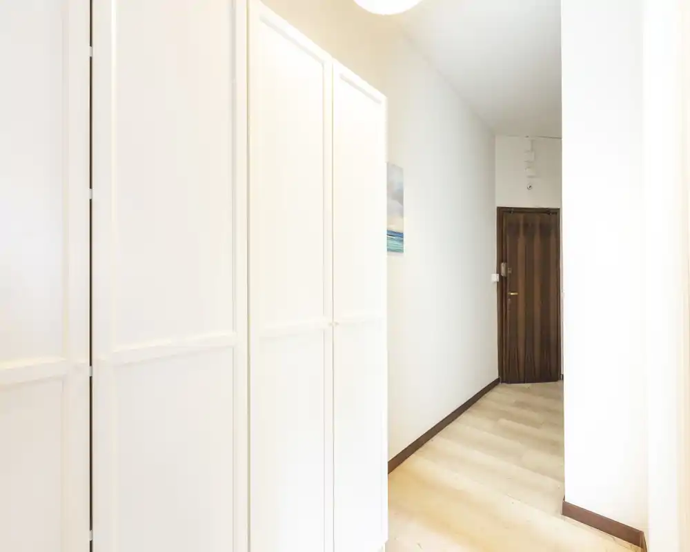 Bright, clean entrance hallway with built-in white wardrobes and a wooden entry door, well lit and welcoming.