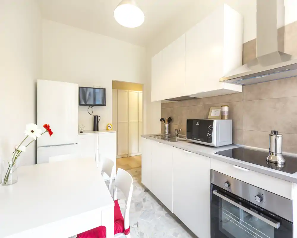Modern, bright kitchen with white cabinetry, built-in oven, microwave and dining table beside the preparation area — a clean, functional space ideal for short-term rentals.