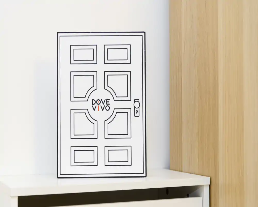 A close-up of a decorative framed print depicting a stylized door placed on a white cabinet beside a wooden panel; minimalist, neutral styling good for product or decor shots.