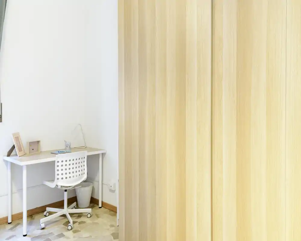 Bright, minimal home office corner with a white desk and swivel chair beside a light wood built-in wardrobe — a neat, functional workspace suitable for remote work.