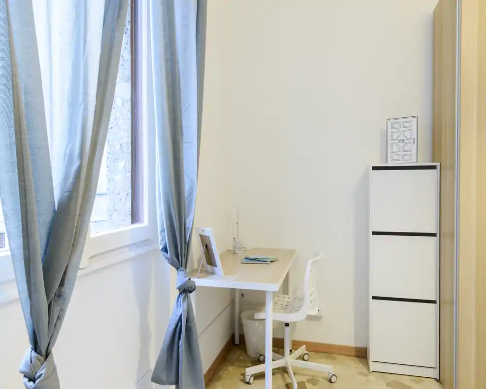 Compact, bright workspace by a window with a simple desk, chair and storage cabinet — ideal for remote work or study in a small apartment.