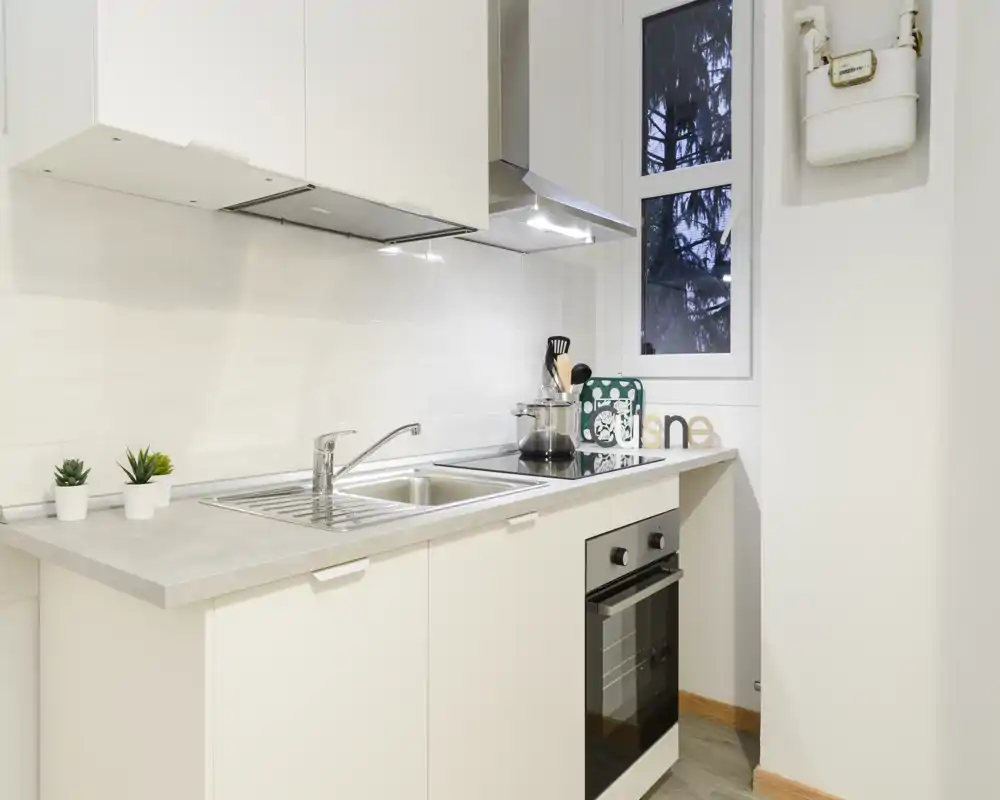 Bright, modern compact kitchen with integrated oven, stainless sink and minimalist white cabinets — clean styling ideal for short-term rentals.
