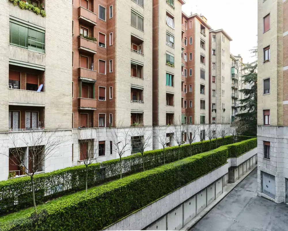 Exterior courtyard view of an apartment block with trimmed hedges, ground-level garages and multiple balconies—useful for showcasing building surroundings and communal outdoor space.