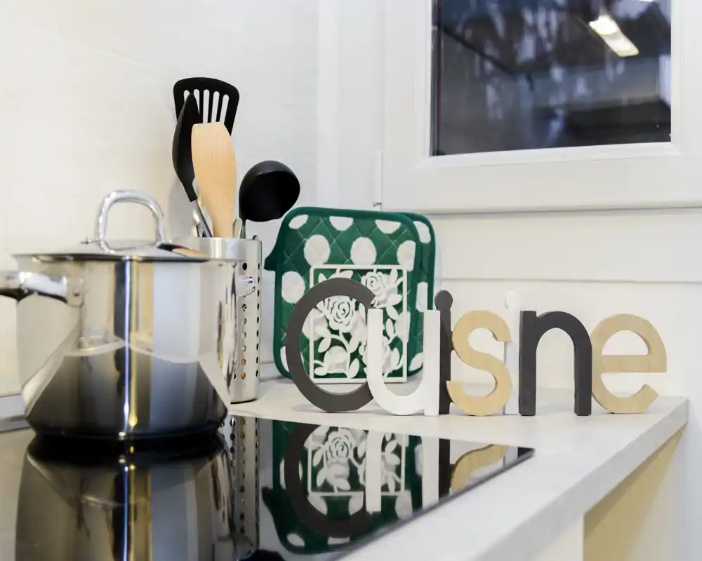 Bright, styled kitchen countertop with a stainless pot, utensil holder, decorative potholder and wooden décor letters, ideal for an attractive cooking corner.