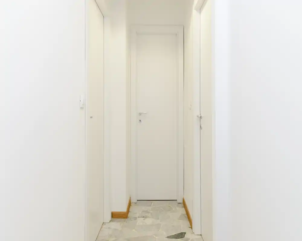 Clean, narrow entrance corridor with white walls, light doors and tiled floor — suitable as a simple hallway or access area.