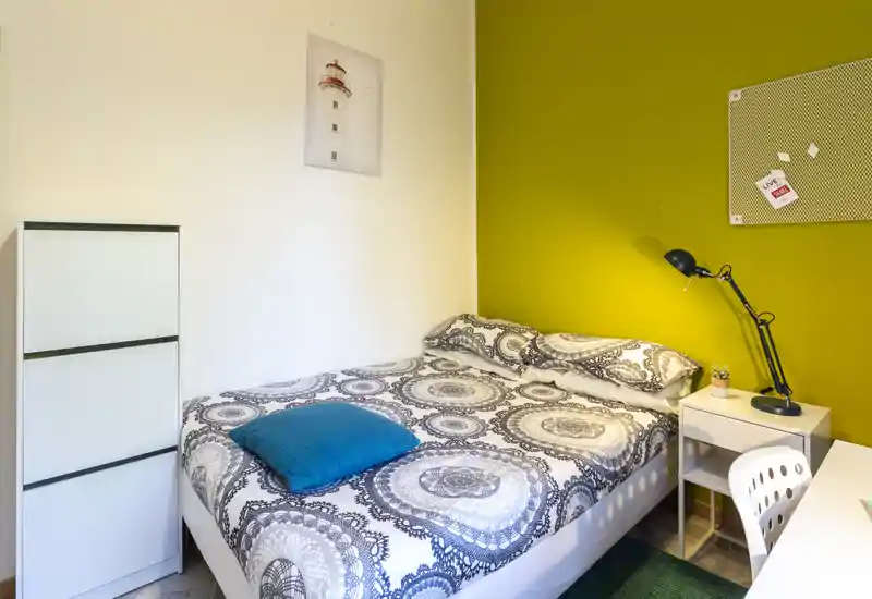 Camera luminosa e ordinata con letto con biancheria decorata, comodino e lampada da tavolo—ideale per un soggiorno confortevole.