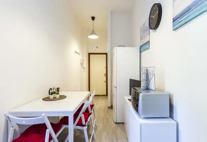 Compact kitchen-dining corridor with a white table and folding chairs, refrigerator and microwave along the wall; bright and tidy space ideal for a small apartment.