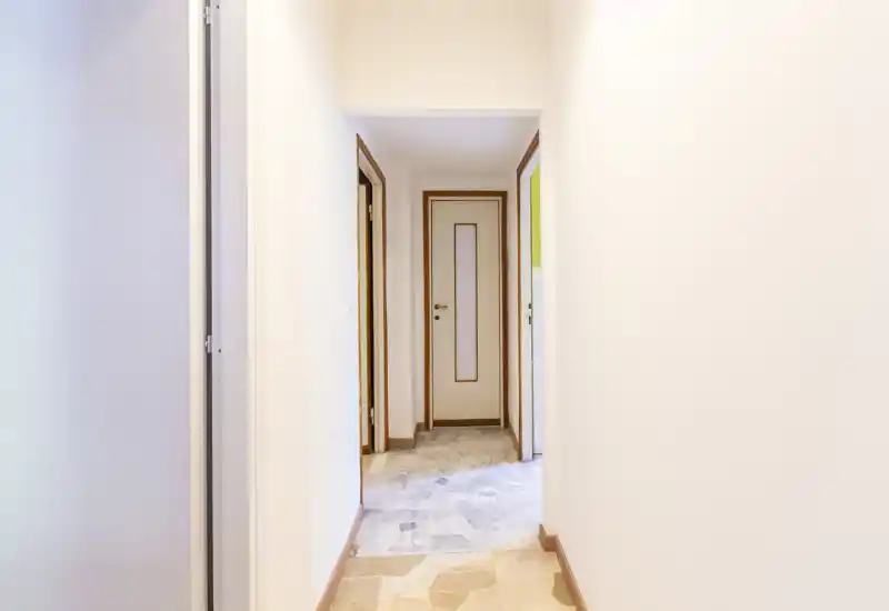 Bright, narrow hallway with tiled floor and multiple interior doors leading to other rooms — clean and well-lit entrance corridor.