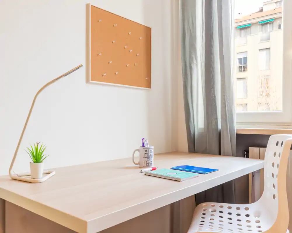 Area studio minimal e luminosa con lampada, piccola pianta e finestra che offre luce naturale — un angolo ordinato ideale per studio o lavoro da remoto.