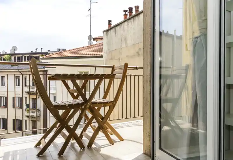 Balcon ensoleillé avec une petite table bistro en bois et deux chaises pliantes, donnant sur les bâtiments voisins — idéal pour un café le matin ou une soirée paisible.