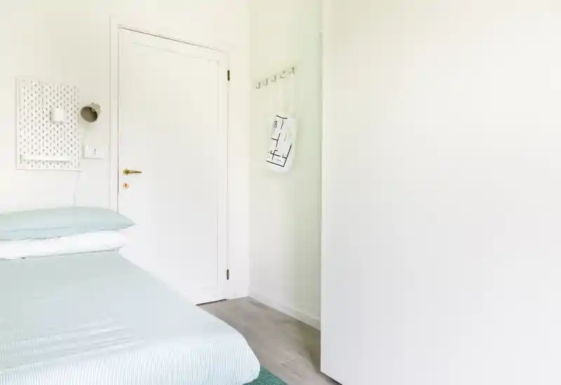 Chambre lumineuse et minimaliste avec un lit bien fait en tons pastel et une armoire blanche. L'espace paraît aéré et apaisant grâce à la lumière naturelle et à la décoration simple.
